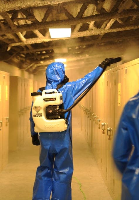 Technician in protective suit spraying odor treatment